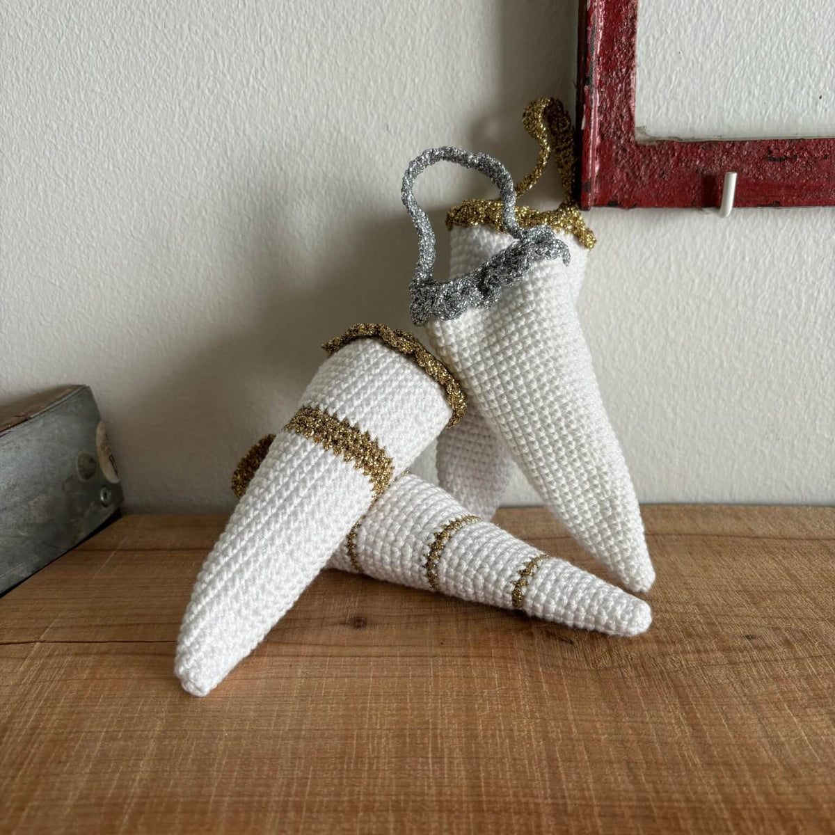 To hæklede kræmmerhuse i hvid med guld- og sølvkant, lænet mod hinanden