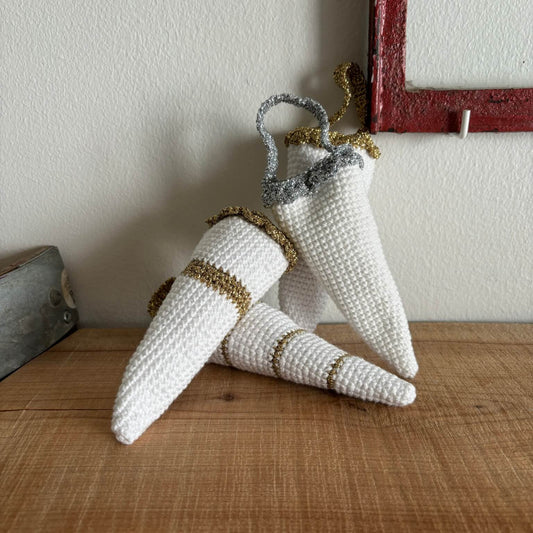 To hæklede kræmmerhuse i hvid med guld- og sølvkant, lænet mod hinanden