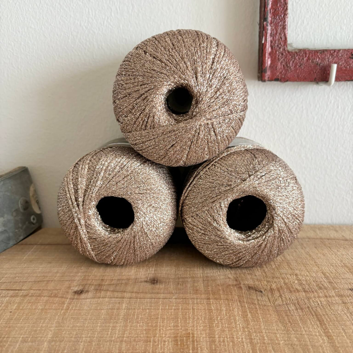 Tre garnnøgler Lurex glimmergarn i beige, stablet