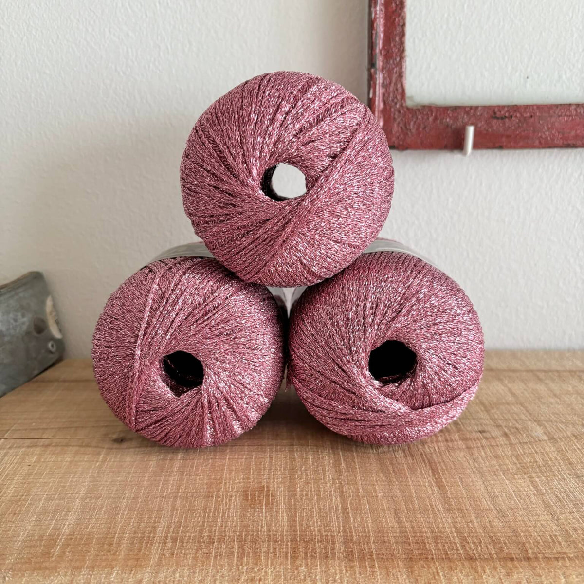 Tre garnnøgler Lurex glimmergarn i rosa, stablet
