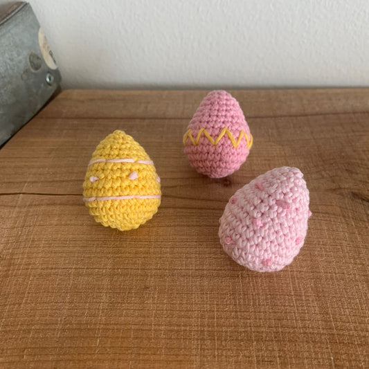 Tre hæklede påskeæg i gult og pink med striber og prikker